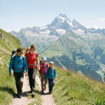 Une famille composée d’un homme, d’une femme et de deux enfants marche sur un sentier herbeux au-dessus de la vallée d’Ossau, avec le pic du Midi d’Ossau en arrière-plan sous une lumière claire d’été.